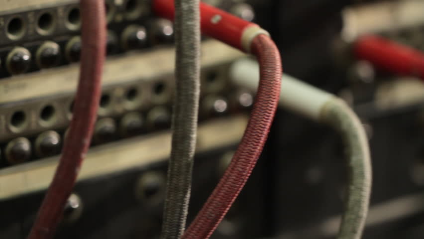 Dolly across an old switchboard.  Hand reaches in and plugs in a cable.