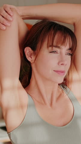 Vertical video, Young woman stretching in her apartment after waking up. She is wearing comfortable workout clothes, awakening her body, and practicing mindfulness and wellness