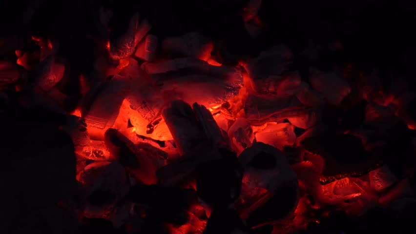 Glowing charcoal embers burning brightly in a grill, ready for cooking. Warm orange and red hues with visible heat and smoke creating a classic barbecue atmosphere.

