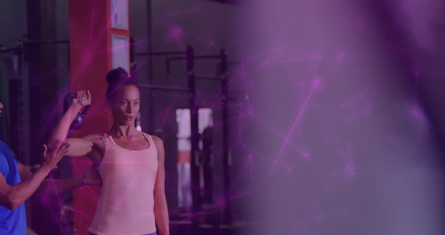 Client gripping kettlebell pressing overhead with gym trainer ensuring form with purple effect. Strength, fitness, training, workout, muscles, motivation, performance