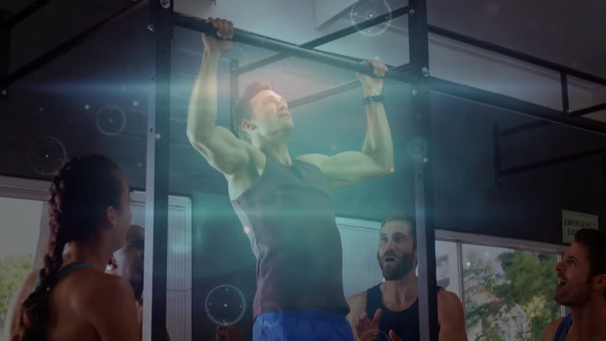 Mid adult man gripping pull-up bar, pulling up in gym, overlaying fitness metrics as group claps. Strength, teamwork, motivation, digital analytics, performance, camaraderie, training
