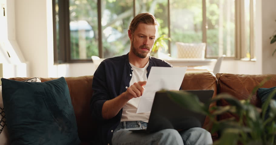 Man, documents and thinking with laptop on sofa for finance, expenses or mortgage bills at home. Male person, wonder or reading with paperwork on computer for financial planning, fund or debt review