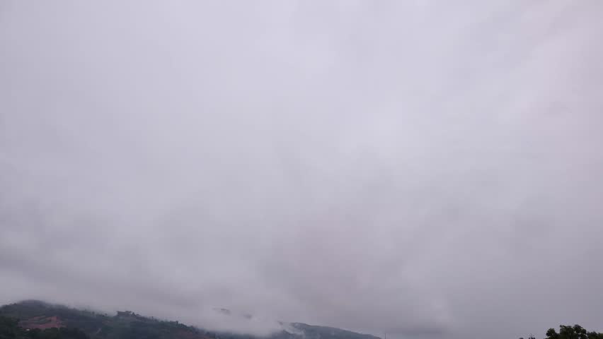 Lush green field under cloudy sky with gentle rain falling, capturing the serene beauty of rural hills and nature during a calm rainy day.