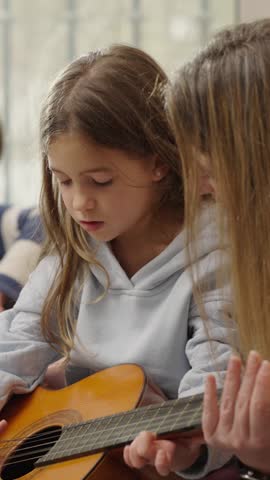 Dedicated music instructor guiding young female student in developing guitar-playing skills during intimate acoustic lesson at home