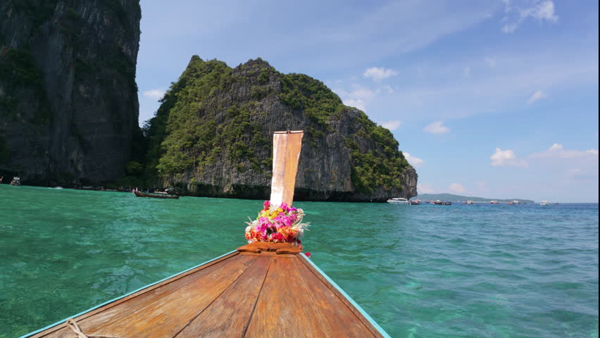 Boats glide through turquoise waters, surrounded by green cliffs in Phuket, Thailand.