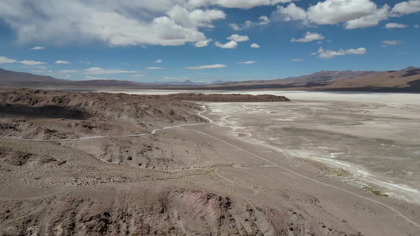 A drone view of the vast rugged landscape of Uyuni Salt Flat with terrain under blue sunny sky with white clouds in Bolivia