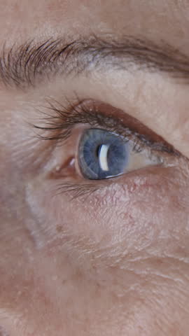 Vertical close up shot of blue eye of mature woman with fine lines on her face