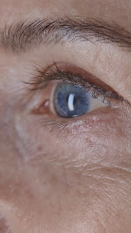 Vertical close up shot of blue eye of mature woman with fine lines on her face