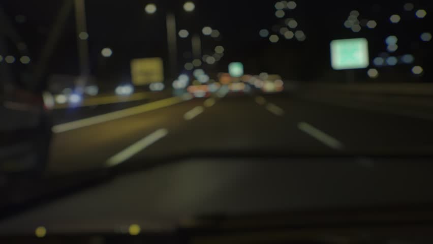 Blurred night video of a speeding ambulance with flashing lights moving through traffic, captured from behind in a dramatic pursuit view