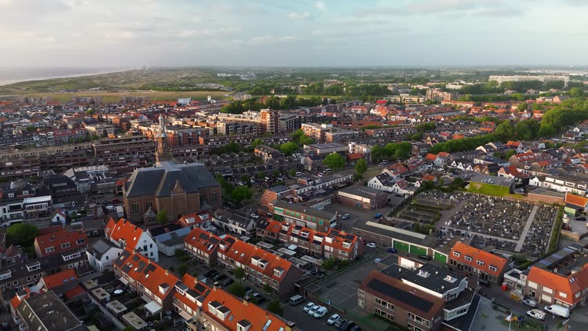 Aerial view of a Dutch town with a prominent church in the center, surrounded by residential homes, green trees, and a clear blue sky on a bright spring day. Peaceful and charming atmosphere.