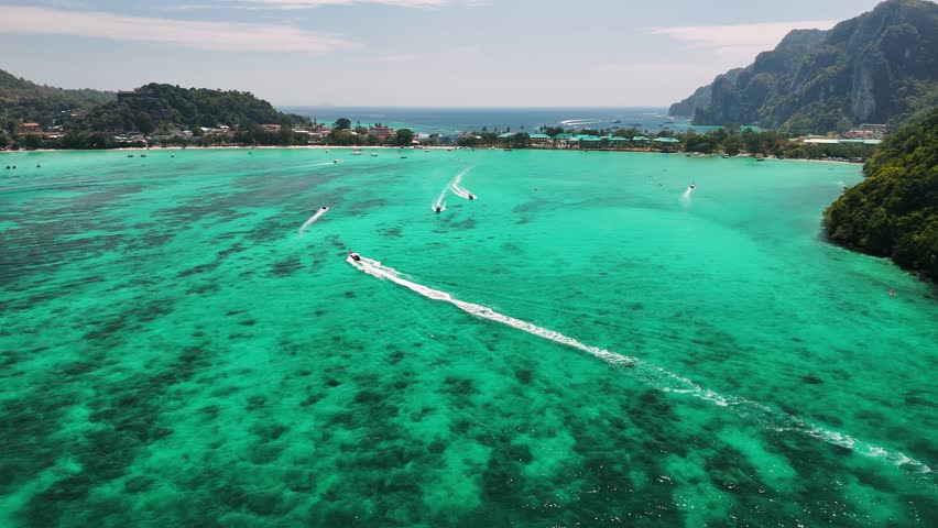 Aerial view of Maya bay, turquoise waters, traditional longtails boats floating near Phi phi island shoreline, Thailand