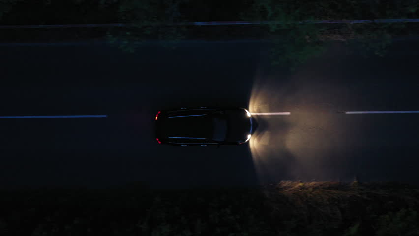Aerial top down view of black car on the road at night