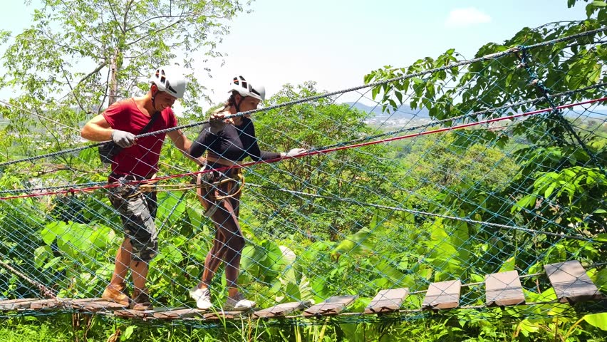 A man and a woman is walking across a challenging ropes course in the extreme park