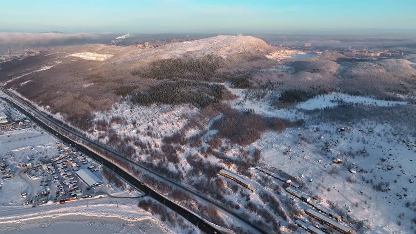 Aerial view showcasing a winter landscape near Murmansk, featuring a long road winding through snow-covered forests, Russia