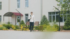 Teenage boy walking alone through the schoolyard holding a book and backpack, captured full body in a natural setting outside the school during daytime - Powered by Shutterstock - Get 15% off with code: PIKWIZARD15
