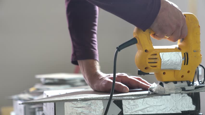 A worker holds an electric jigsaw in his hands and cuts quartz vinyl in an apartment. Apartment renovation work with a saw. Cutting tiles indoors. High quality 4k footage