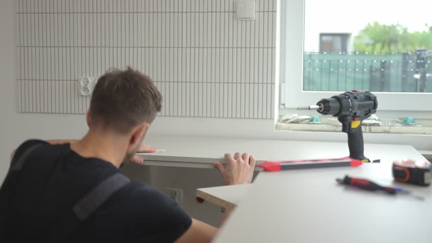Man uses spirit level to align kitchen countertop panel during installation. Professional kitchen furniture assembly during renovation in new home