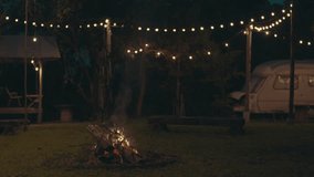 Camper is enjoying a bonfire near his cozy travel trailer in an autumn forest at night, Serene scene of a caravan with a campfire and string lights surrounding, set in a calming forest at dusk - Powered by Shutterstock - Get 15% off with code: PIKWIZARD15