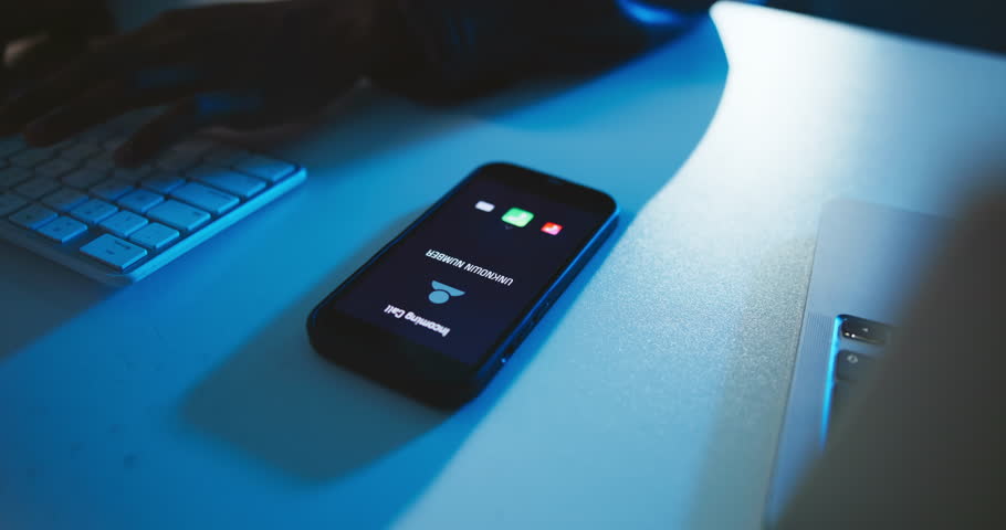 Hands, typing and incoming call with phone screen in office with unknown number, phishing scam or ignore spam at night. Computer, person or cell with private contact for mobile fraud and late scammer