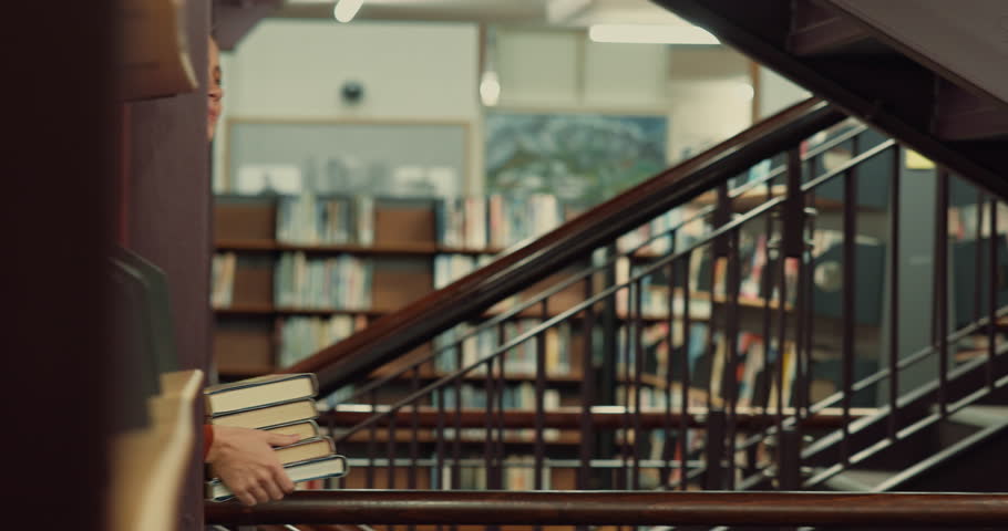 Woman, student and walking in library with books for learning, education or study material. Female person, academic scholar or learner with textbook or novel pile for story or knowledge at university