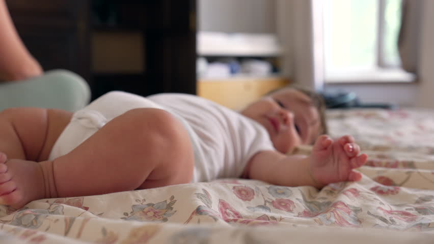 Baby attempting to roll on bed with mother’s gentle push, early motor skills development, playful effort, sensory exploration, home environment, growth, encouragement