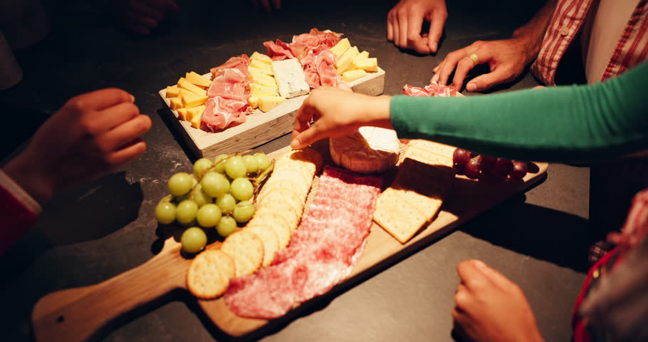 Snacks, hands and people eating from charcuterie board at night for dinner, nutrition and hungry. Above, friends and food selection for social gathering, organic diet and healthy meal at party