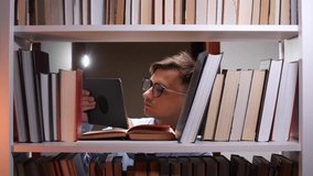 Student reading tablet and books between shelves in library at night - Powered by Shutterstock - Get 15% off with code: PIKWIZARD15