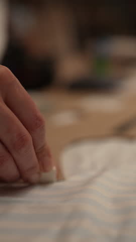 Vertical cropped shot of artisan tracing sewing pattern onto cardboard using chalk in dressmaking workspace. Fashion designer drafting cardboard sewing patterns, aligning templates, slow motion.