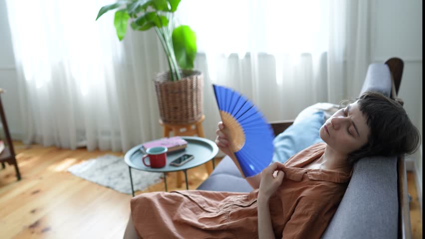 Weary exhausted woman fanning herself struggling with unbearable temperatures, heat exhaustion and dehydration, airless environment, health deterioration, vulnerability to high heat, no conditioning