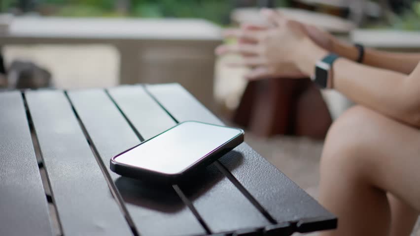 Over the shoulder view of a woman taking a photo of a flower with her smartphone in a lush garden.