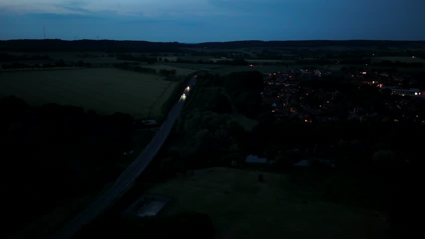 Driving vehicles on dark suburb interstate road of United States. Lighting headlights of vehicles on rural highway. Aerial wide shot at dusk. Lighting cityscape of small city.