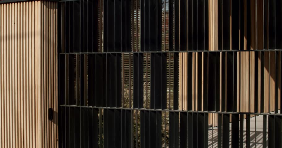 Modern black metal fence gate with vertical wooden panels. Stylish architectural design. Contemporary entrance, privacy, and security. Urban or suburban property. Exterior, minimalist aesthetic