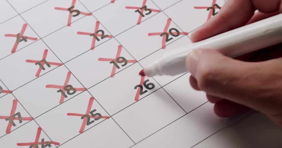 Close-up of a hand using a red marker to cross out dates on a calendar, signaling a countdown. Concept of planning, schedule, and time management.
