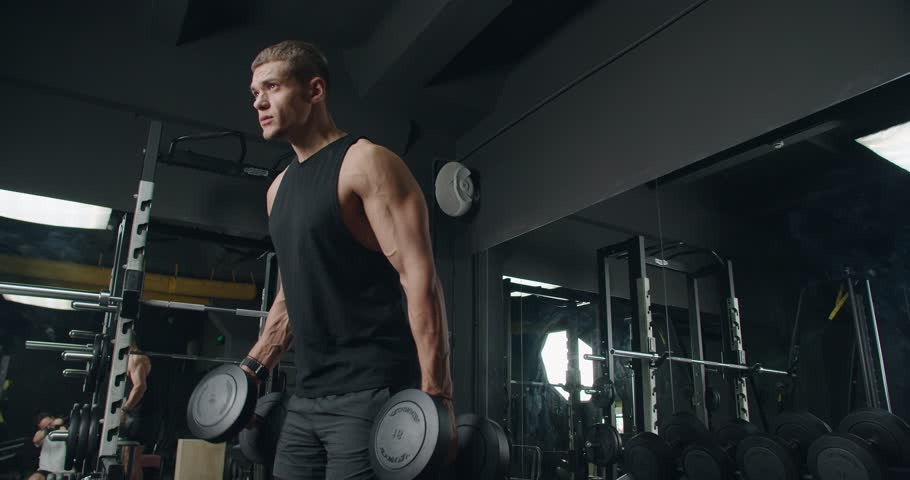 Young Athletic Man Lifting Weights in a Modern Gym. Focused young adult male lifting dumbbells in a well-equipped gym, displaying strength and determination.