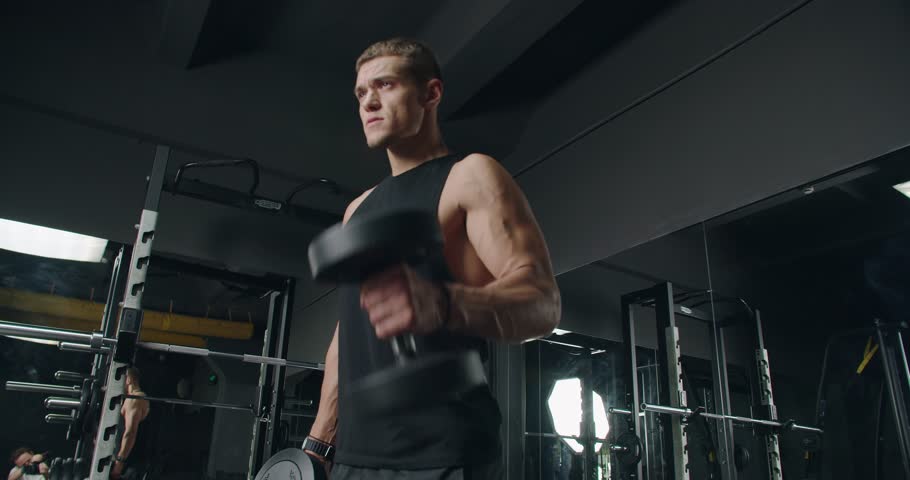 Young Athletic Man Lifting Weights in a Modern Gym. Focused young adult male lifting dumbbells in a well-equipped gym, displaying strength and determination.