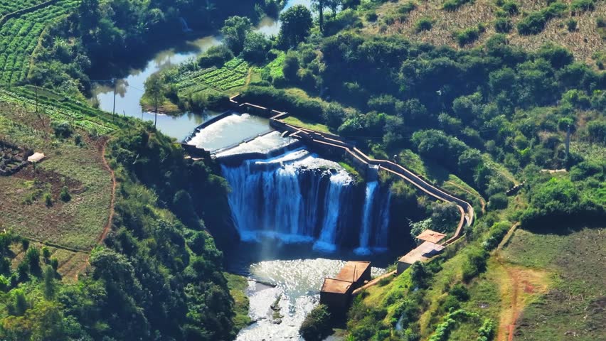 Drone shot of a cascading waterfall surrounded by vibrant farmland and lush green vegetation in Madagascar. Scenic rural landscape ideal for eco-travel, agriculture, or nature projects.