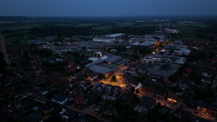 Aerial establishing shot of illuminated roundabout in american town. Wide shot. Warehouse with Buildings in industrial district. Houses and homes of neighborhood at dusk. Night scene in USA.