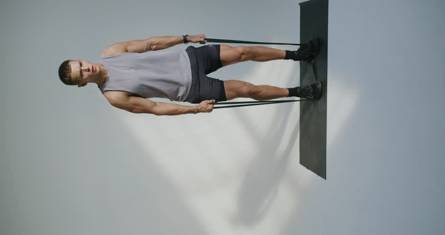 Athletic man works out using resistance bands in a studio, demonstrating strength and fitness. Young Athlete Engaging in Resistance Band Training in a Studio Setting. Vertical video.