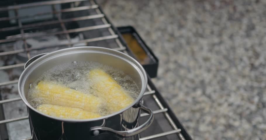Boiling corn on the cob outside on a camp stove 