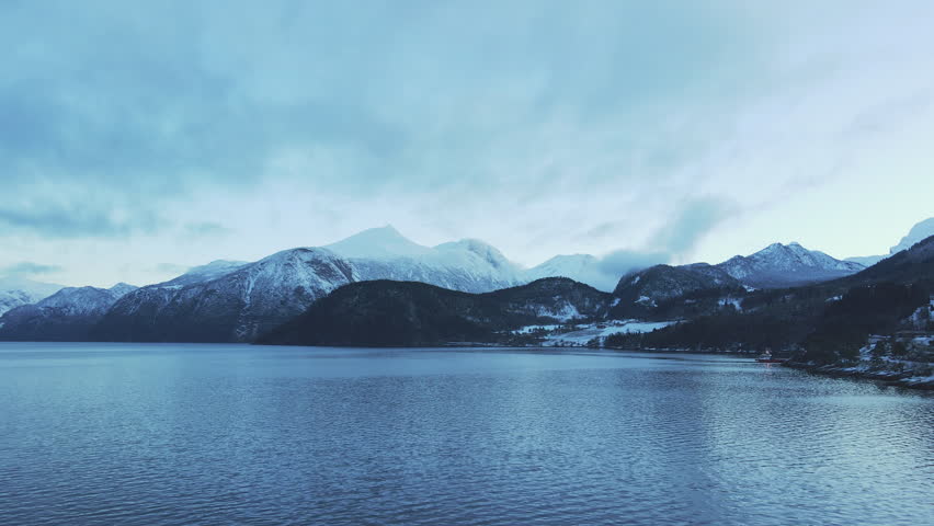 Drone flying over a fjord in Sunnmøre, Norway in winter time. Looking towards mountains covered in snow.