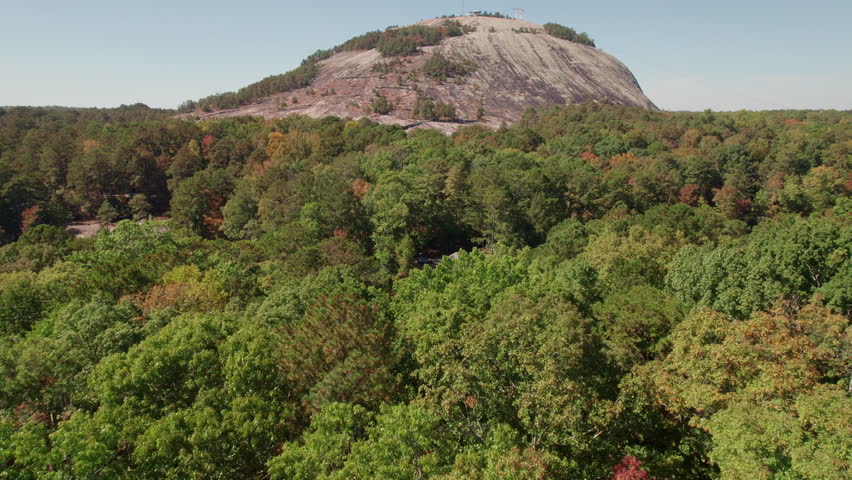 A cinematic aerial flyover the lush tree canopy and river approaching Stone Mountain in the popular state park for hiking, tourism, kayaking, cycling, and outdoor recreation in Georgia.