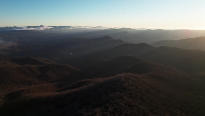 A slow cinematic aerial with warm morning light casting rays and shadows over rolling hills of the Blue Ridge mountain range in Georgia, a popular hiking and tourism region in the southeast.