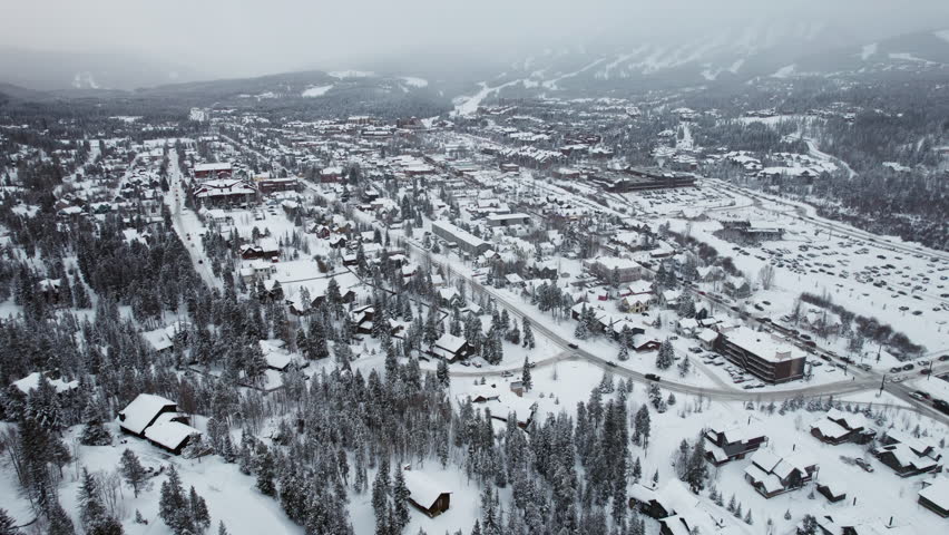 A wide establishing aerial of Breckenridge, Colorado, peaceful, beautiful and snow-covered in winter, with cars carrying skis and snowboards into the popular mountain town and world famous resort.