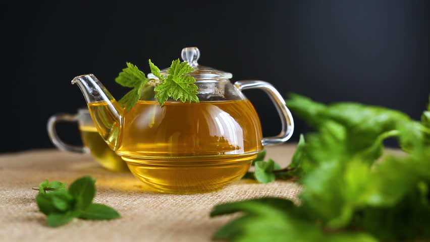 Green tea with currant leaves and mint in glass teapot and cup on black background