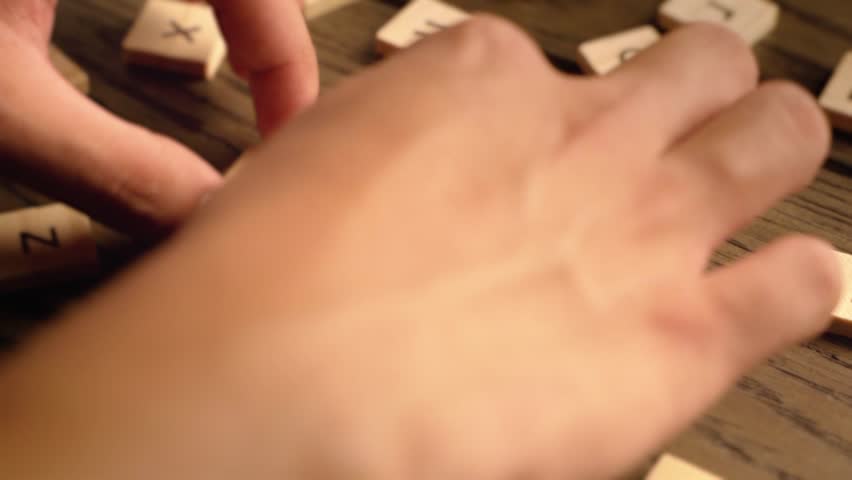 A hand arranges wooden letter tiles to spell the word care on a warm-toned wooden table.