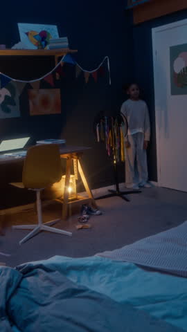 Vertical full shot of joyful little Black girl playing hide-and-seek with funny alien monster in her cozy room in evening
