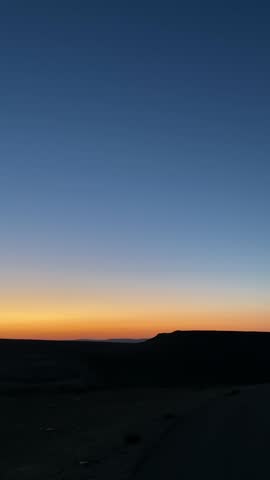 Pan across empty desert terrain with mountains and plains during sunset or sunrise with colorful romantic sky with warm orange and yellow. Dusk or dawn in natural landscape view user content style