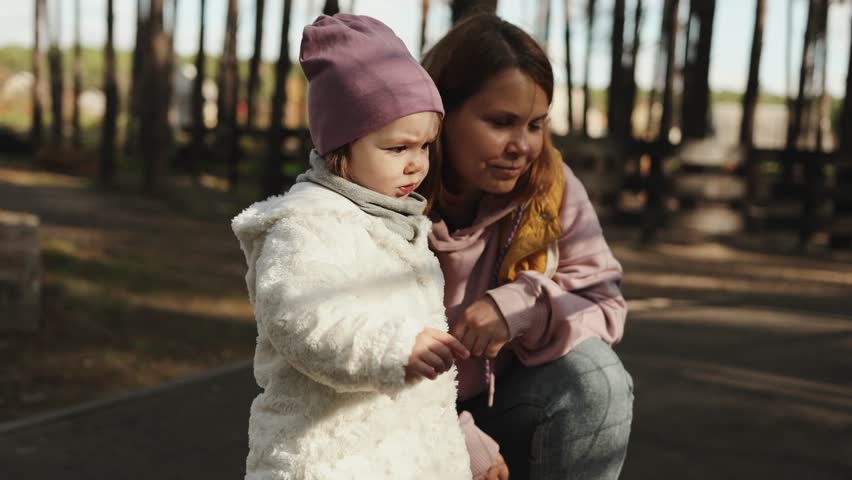 Mother and her little daughter happily enjoying the beauty of nature in the autumn park, chatting in a serene forest setting. Happy childhood, sunny day, family day.