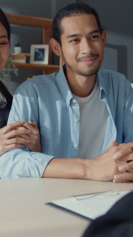 Vertical Screen : Happy asian young customer couple ready sign bank loan agreement for new house with broker agent, husband and wife consider finance investment insurance contract in front of broker.