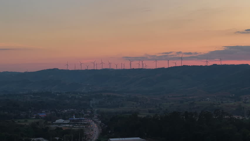 drone captures scenic highland landscape of Khao Kho Phetchabun Thailand with wind turbines spinning slowly during colorful sunset sky showing renewable energy and tranquil rural countryside
